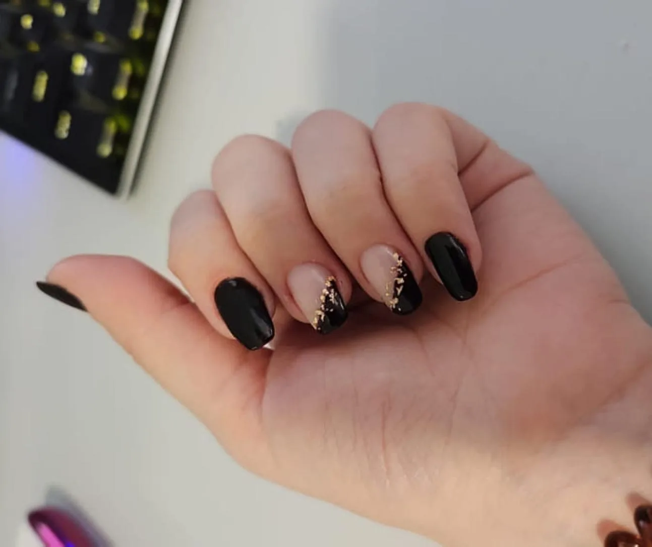 Black nude and gold-flake nail art with polish rack behind