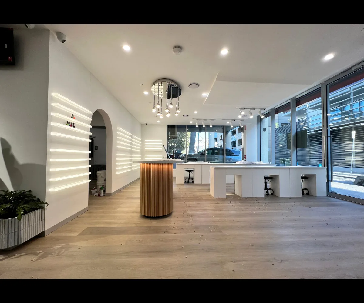 Bright salon during fitout — wood-slat counter and LED shelving visible, white manicure benches