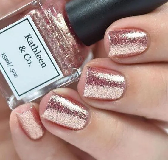 Rose-gold glitter nails beside a nail polish bottle