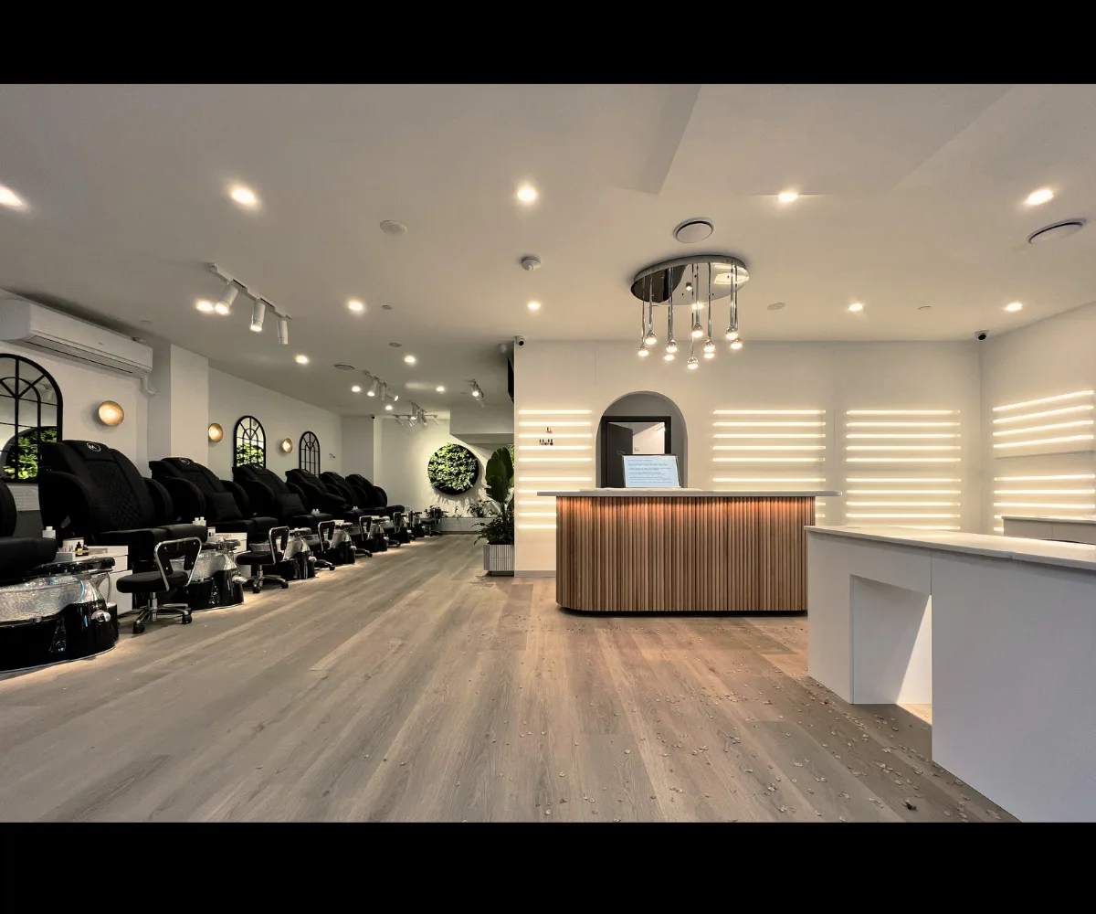 MONSTERA reception — curved honey-wood counter, LED back-lit shelving, white arched doorway, circular plant feature
